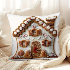 a decorative gingerbread house pillow sitting on a couch next to a white throw pillow