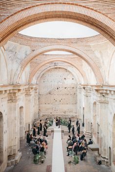 an outdoor ceremony with people sitting and standing in the aisle, surrounded by stone arches