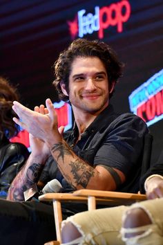 a man with tattoos sitting in a chair and smiling at the camera while holding his hands up