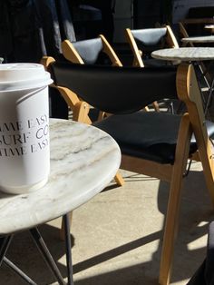 a white coffee cup sitting on top of a marble table next to black folding chairs