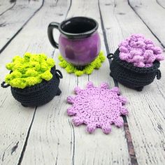 three crocheted pot holders sitting on top of a wooden table next to a mug