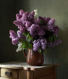 a vase filled with purple flowers sitting on top of a wooden table next to a wall