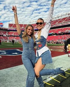 two women in overalls standing on the sidelines at a football stadium with their arms up