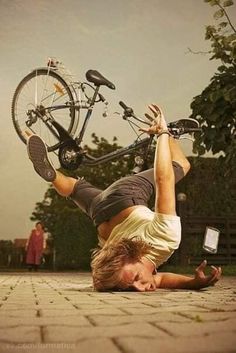 a man doing a handstand on the ground with his bike in the background