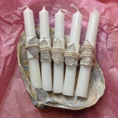 five white candles tied with twine and sitting in a bowl on pink tissue paper