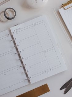 an open planner, scissors and tape on a white table with a pair of scissors next to it