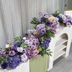 purple and white flowers are in a green vase on a shelf next to a window