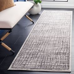 a large rug in the middle of a room next to a couch and chair with a plant on it