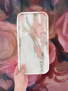 a hand holding a white tray with pink and black paint on it