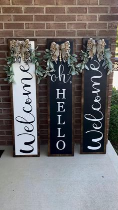 three black and white wooden signs with greenery on the front of a brick building