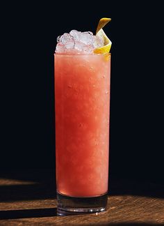 a tall glass filled with watermelon and ice on top of a wooden table