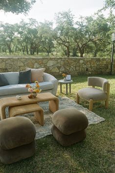 a living room filled with furniture on top of a lush green field next to a stone wall