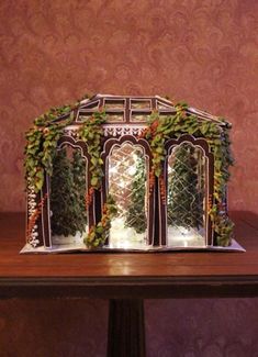 a gingerbread house decorated with greenery and lit candles on a table in front of a wall