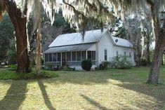 a white house surrounded by trees with moss hanging from the roof and covered in spanish moss