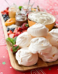 a wooden platter filled with whipped cream and fruit on top of a red table cloth