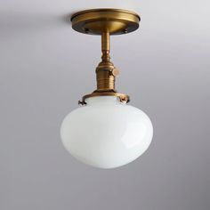 an antique brass ceiling light with a white glass globe hanging from it's side