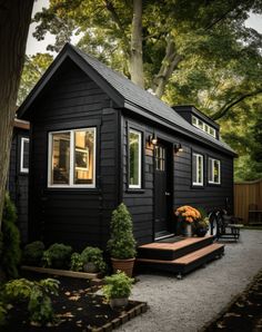 a small black house with lots of windows and plants on the front porch, along with steps leading up to it