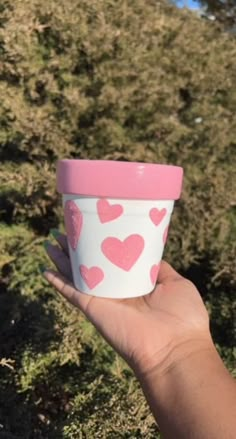 someone holding up a cup with hearts on it in the middle of a grassy field