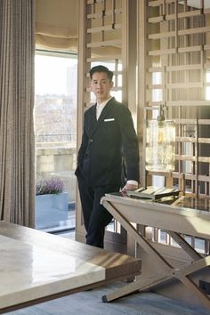 a man standing in front of a table with a book on top of it next to a window