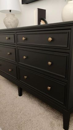 a black dresser sitting on top of a carpeted floor next to a white lamp