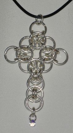 a silver cross on a black cord with a crystal bead hanging from it's center