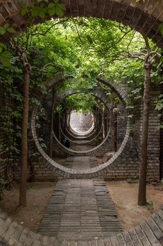 an arched brick wall with trees growing over it in the middle of a walkway between two buildings