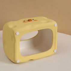 a yellow plastic toy with two faces on it's face, sitting on top of a white table