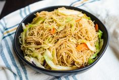 a bowl filled with noodles and vegetables on top of a white table cloth next to a fork