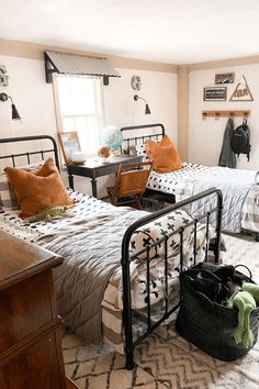 two beds in a room with white walls and black metal frames, one has an orange pillow on the bed