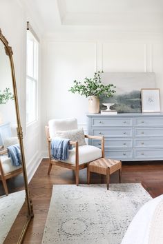 a blue dresser and chair in a white room with wooden floors, large mirror on the wall