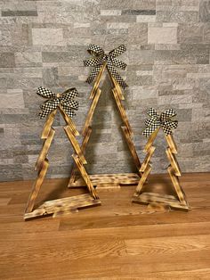 two wooden christmas trees with black and white checkered bows on them, standing in front of a stone wall