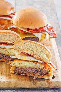 three cheeseburgers on a wooden cutting board with bacon and egg in the middle