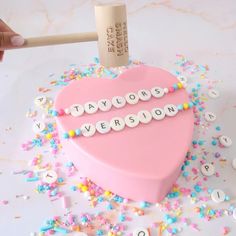 a pink heart shaped cake with words spelled out on it and sprinkles