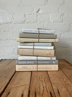 a stack of books sitting on top of a wooden table next to a white brick wall