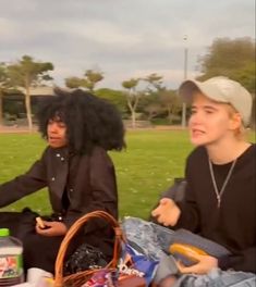 two people sitting on the grass with food and drinks