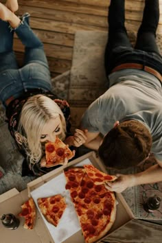 two people eating slices of pizza from a box on the floor next to each other