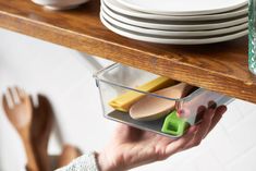 a person holding a container with spoons and spatulas in it on top of a shelf