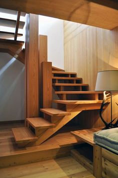 a room with wooden stairs and a bed in it, next to a lamp on a table