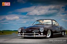 an old black car is parked on the side of the road with clouds in the background