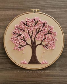 a hand embroidered tree with pink and white flowers on it, sitting in front of a hoop