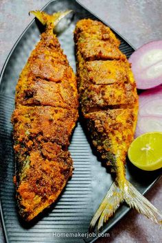 two fish fillets on a plate with lemon wedges and red onions in the background