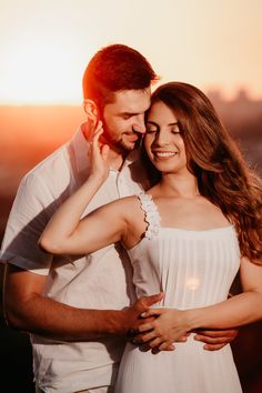 a man and woman standing next to each other in front of the sun at sunset