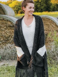 a woman standing in front of hay bales wearing a black and white shawl