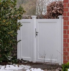 a white gate with a brick wall and shrubbery in the foreground behind it