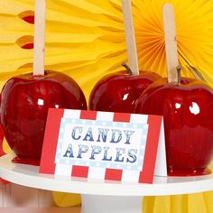 two red apples sitting on top of a white cake stand with candy apples attached to them