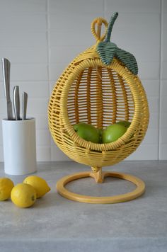 two green apples sitting in a yellow basket next to some lemons and knifes