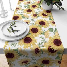 a sunflower table runner with white plates and vases on the table in front of it