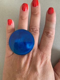 a woman's hand holding a blue ring with red nail polish