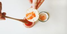 a person holding a spoon over a small cracker with an orange jelly on it