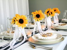 the table is set with sunflowers in vases and place settings for dinner